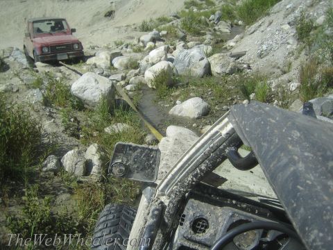 1987 Suzuki Samurai - Two off-road vehicles navigate a challenging, rocky path with a tow strap connecting them.