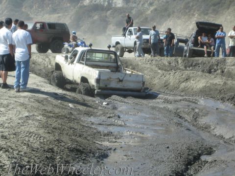 1987 Suzuki Samurai - Multiple off-road vehicles navigate a muddy terrain, with onlookers observing the action.