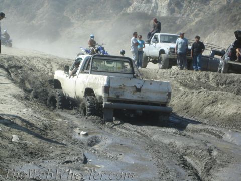 1987 Suzuki Samurai - Several vehicles navigate a muddy off-road course, with one truck deeply stuck in the mire.