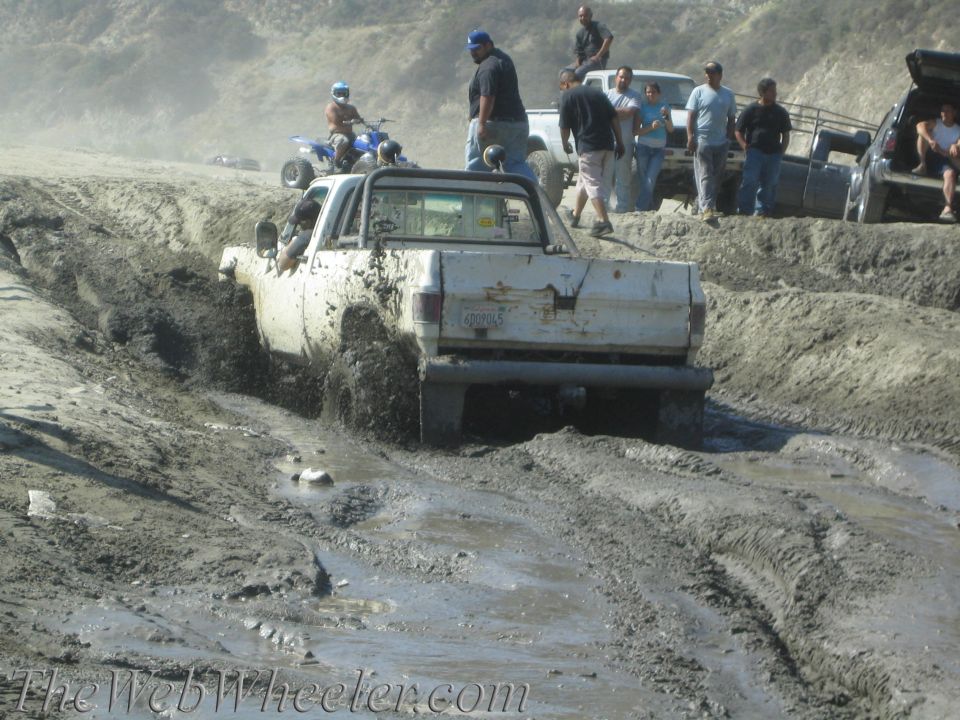 White pickup truck with mud splashing from its wheels, stuck in a muddy track