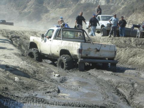 1987 Suzuki Samurai - A group of people and vehicles are off-roading in a muddy, hilly area.