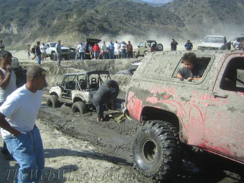1987 Suzuki Samurai - Several off-road vehicles are stuck in the mud, with onlookers observing the scene.