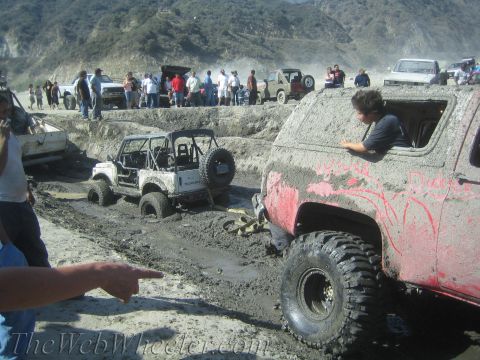 1987 Suzuki Samurai - A Suzuki Samurai is stuck in a mud pit while onlookers watch, with a red SUV also covered in mud nearby.