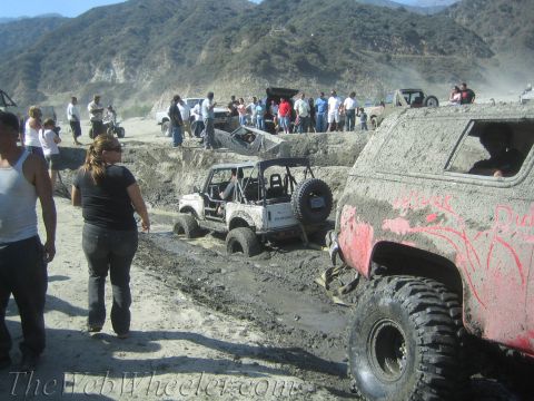 1987 Suzuki Samurai - Several off-road vehicles are stuck in thick mud during an event, with spectators watching.