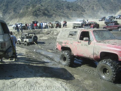 1987 Suzuki Samurai - Several off-road vehicles are stuck in the mud, with a crowd of onlookers observing the scene.