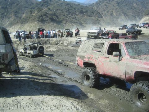 1987 Suzuki Samurai - Multiple off-road vehicles are stuck in mud during an event, with spectators watching from the side.