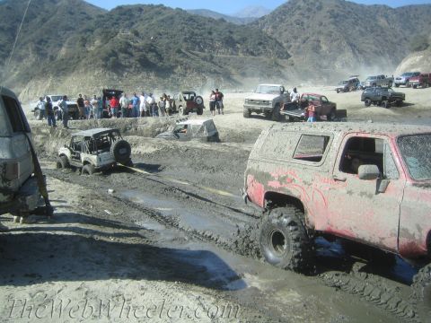 1987 Suzuki Samurai - A group of off-road vehicles are bogged down in a muddy terrain, with spectators observing the scene.