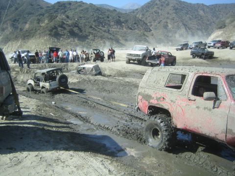 1987 Suzuki Samurai - Multiple off-road vehicles are stuck in the mud, with spectators watching the recovery efforts.