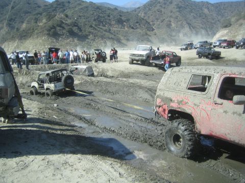 1987 Suzuki Samurai - Multiple off-road vehicles are stuck in the mud and being towed in a challenging terrain.