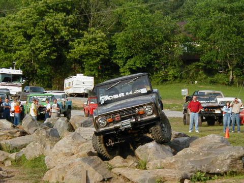 1990 Ford Bronco - A classic Ford Bronco navigates a challenging rock obstacle course with spectators nearby.