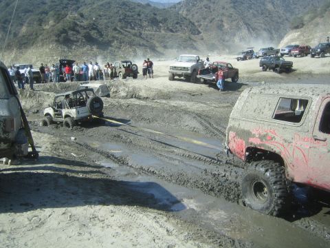 1987 Suzuki Samurai - Off-road vehicles navigate a muddy terrain, with some getting stuck and requiring assistance.