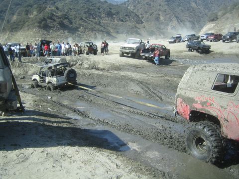 1987 Suzuki Samurai - A group of off-road vehicles are bogged down in a muddy area, with spectators observing the scene.