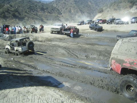 1987 Suzuki Samurai - A group of off-road vehicles navigate a muddy terrain, with one Suzuki Samurai requiring a tow.