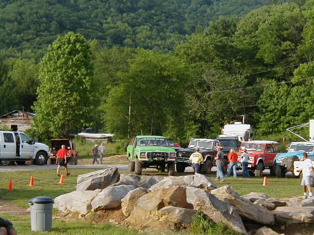 1990 Ford Bronco, green, front view, parked on dirt with rocks and trees