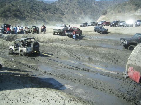1987 Suzuki Samurai - A group of off-road vehicles are navigating a challenging muddy terrain, with some vehicles requiring assistance.