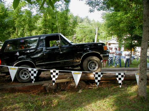 1990 Ford Bronco - A black SUV navigates an obstacle course, with spectators watching in the background.