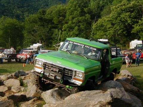 1990 Ford Bronco - A green Ford Bronco navigates a rocky obstacle course, with other vehicles and trees in the background.