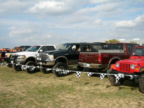 1978 Ford Bronco - Several modified trucks and SUVs are parked in a row, with checkered flags decorating the front of the line.