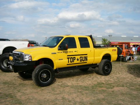 1978 Ford Bronco - This yellow Ford F-Series truck features "Top Gun" graphics and a lifted suspension, seen at an outdoor event.