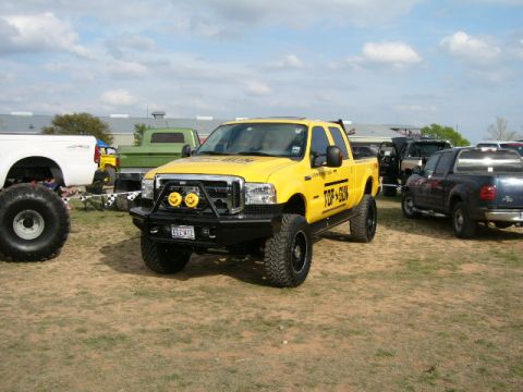 1978 Ford Bronco - A lifted yellow Ford F-250 truck with custom bumper and smiley face lights is parked in a lot with other vehicles.