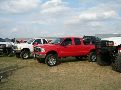 1978 Ford Bronco - Several pickup trucks are parked on a grassy field under a cloudy sky.