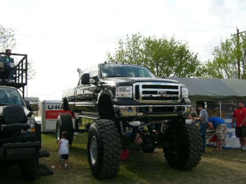 1978 Ford Bronco - Modified black Ford pickup truck on display with massive tires and lifted suspension.