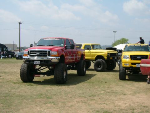 1978 Ford Bronco - A red Ford F-250 truck is parked on a grassy field with other vehicles.