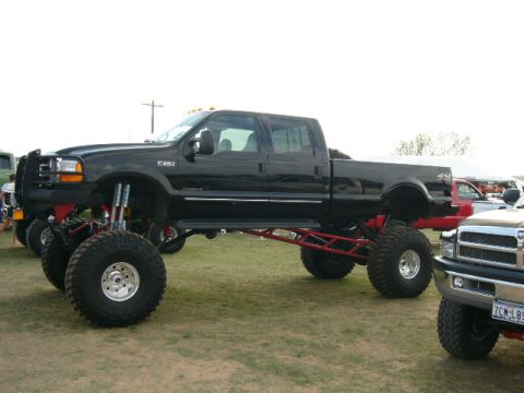 1978 Ford Bronco - Custom lifted black Ford F-350 Super Duty pickup truck with large off-road tires and red suspension.