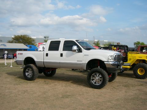 1978 Ford Bronco - A lifted white pickup truck is parked next to a yellow off-road vehicle under a partly cloudy sky.