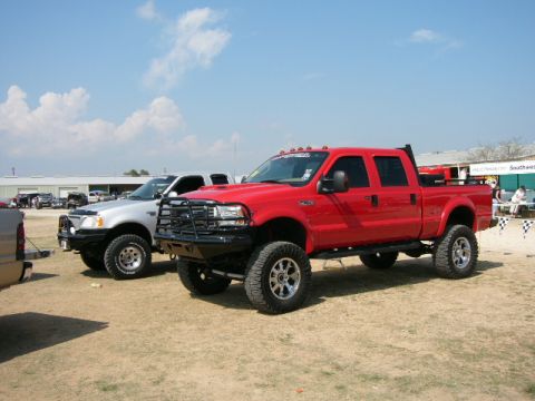 1978 Ford Bronco - Two lifted pickup trucks, a red Ford F-250 and a silver Ford F-150, are parked outdoors on a sunny day.