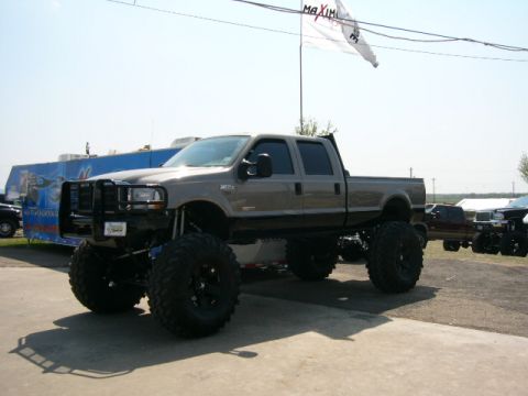 1978 Ford Bronco - A heavily modified pickup truck with oversized tires is parked outdoors, with other vehicles in the distance.