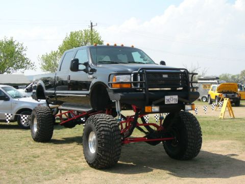 1978 Ford Bronco - A heavily modified black pickup truck with oversized tires and a custom front bumper is displayed at an outdoor event.