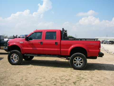 1978 Ford Bronco - Side view of a red pickup truck with large tires and a custom bed rack.