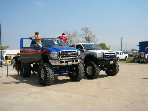 1978 Ford Bronco - Two custom lifted Ford trucks are parked side-by-side under a clear blue sky.