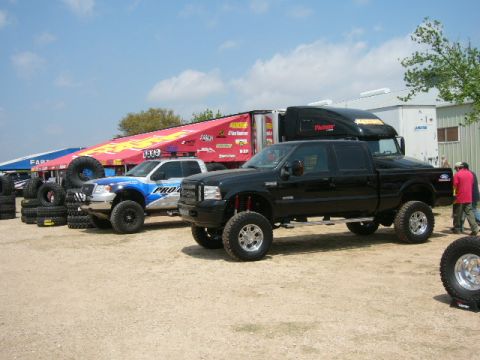1978 Ford Bronco - A black lifted pickup truck is parked at an outdoor event with other vehicles and tents in the background.