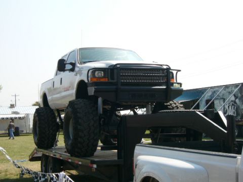 1978 Ford Bronco - A heavily modified white pickup truck with oversized tires is loaded onto a trailer.