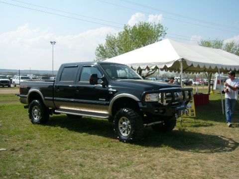 1978 Ford Bronco - A black Ford F-250 Super Duty pickup truck is parked on a grassy field near a large white tent.