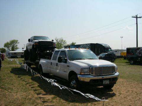 1978 Ford Bronco - White Ford F-350 dually truck transports a lifted Ford F-Series truck on a trailer.