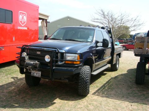 1978 Ford Bronco - A blue Ford F-250 Super Duty pickup truck is parked next to a red Dodge trailer at an outdoor event.