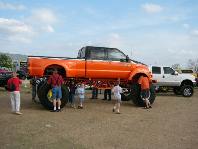 Massively lifted orange Ford F-250 Super Duty show truck with crowd around it