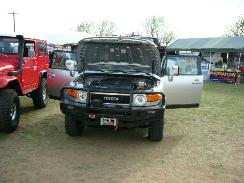 1978 Ford Bronco - Two off-road vehicles are parked on grass, with tents and vendor displays in the background.