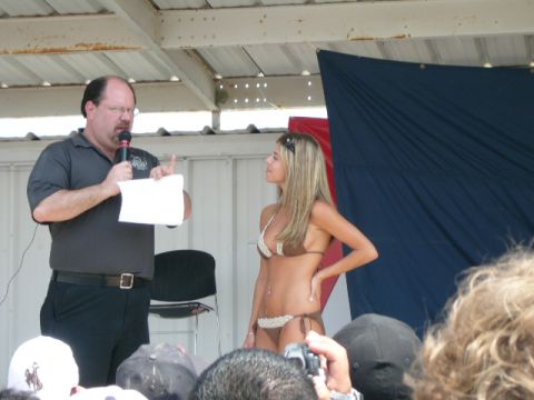 1978 Ford Bronco - A man addresses a crowd while a woman in a bikini stands beside him on a stage.