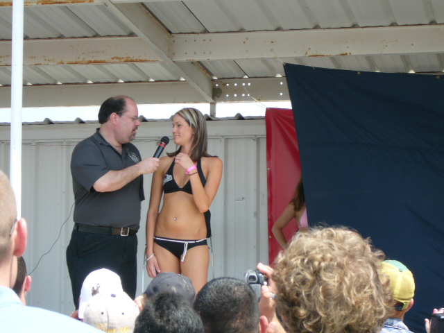 Woman in black bikini on stage with interviewer, crowd in foreground