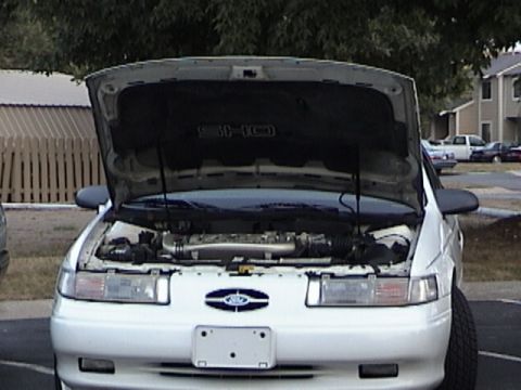 1993 Ford Taurus - The front of a white 1993 Ford Taurus SHO is shown with its hood open, revealing the engine compartment.