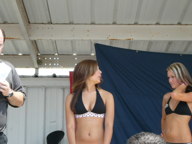Man holding paper, two women in bikinis on stage