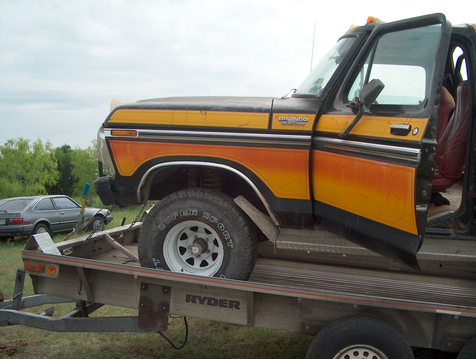 1978 Ford Bronco with orange and yellow stripes on a trailer, another car visible behind it