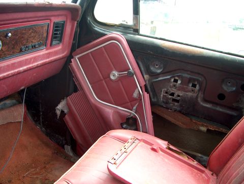 1979 Ford Bronco - Interior view of a 1979 Ford Bronco, showing red upholstery, wood-grain trim, and a damaged door panel.