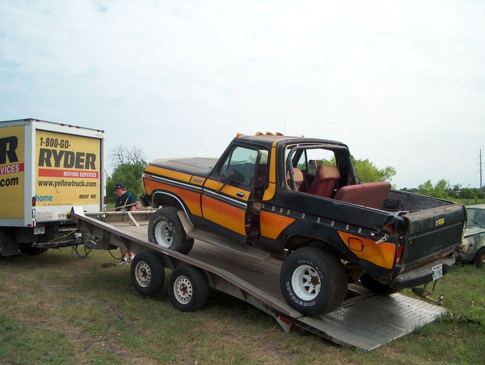 Black and orange 1978 Ford Bronco on a trailer, being towed by a Ryder truck
