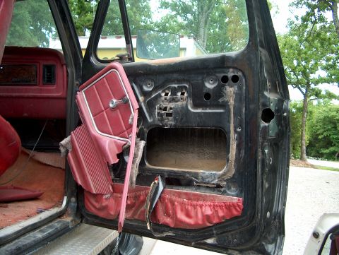 1979 Ford Bronco - The interior door panel of a vehicle, showing red upholstery and the exposed inner workings of the door.
