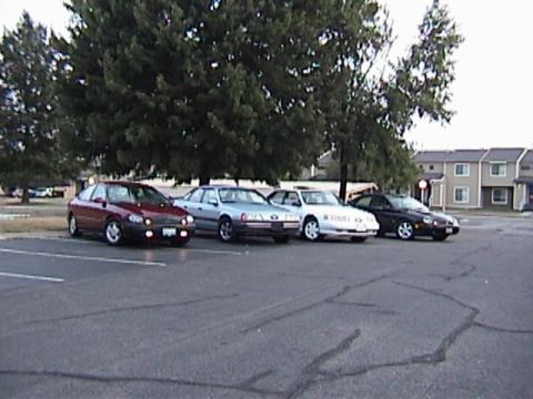 1993 Ford Taurus - Several sedans are parked in a lot, with trees and apartment buildings visible.